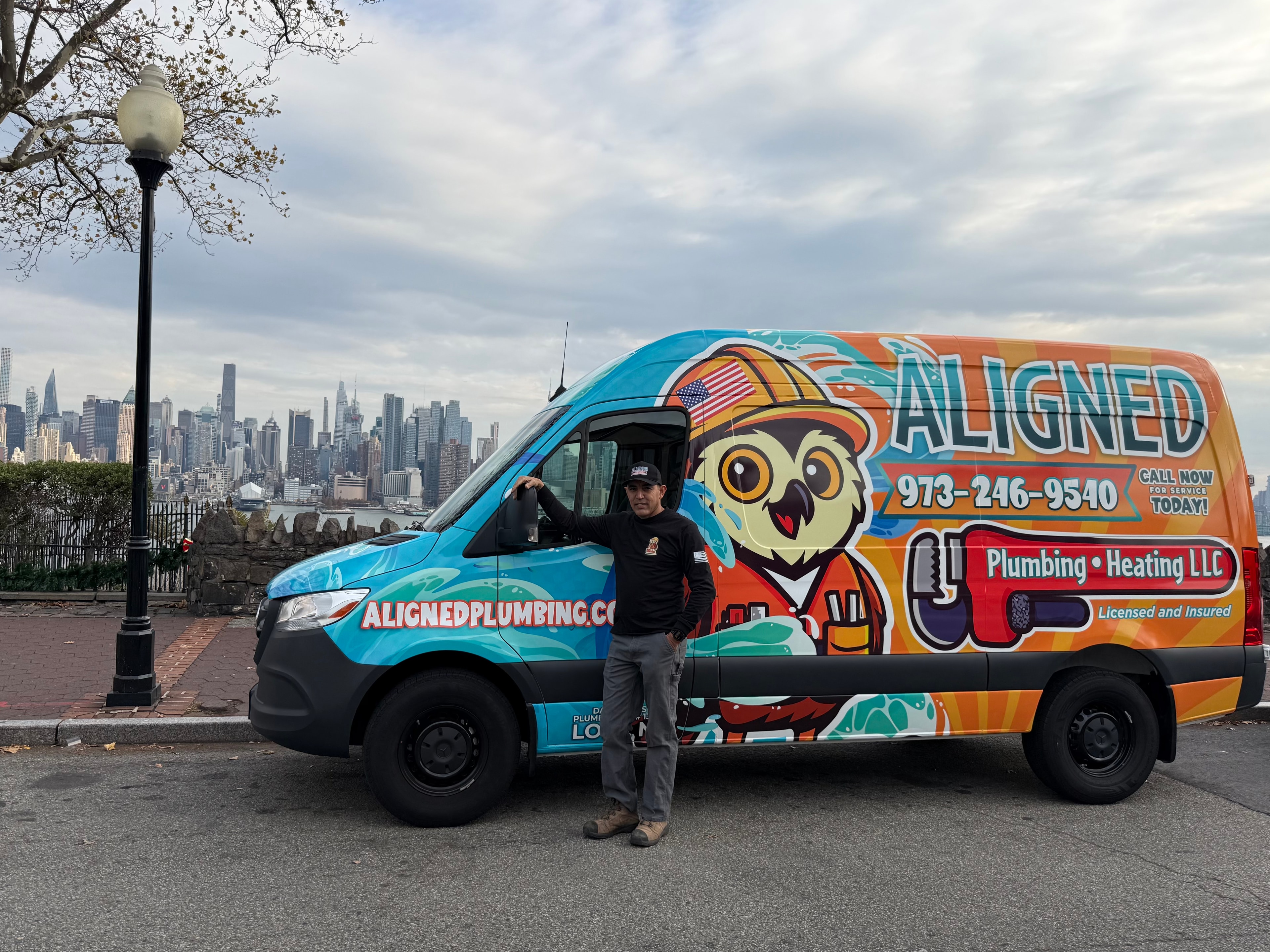 David Elias beside the Aligned Plumbing & Heating van, with the Manhattan skyline behind him