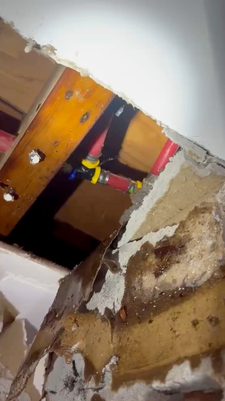 Video of water dripping from a red PEX pipe fitting between ceiling joists, above a water-damaged ceiling that has been opened up