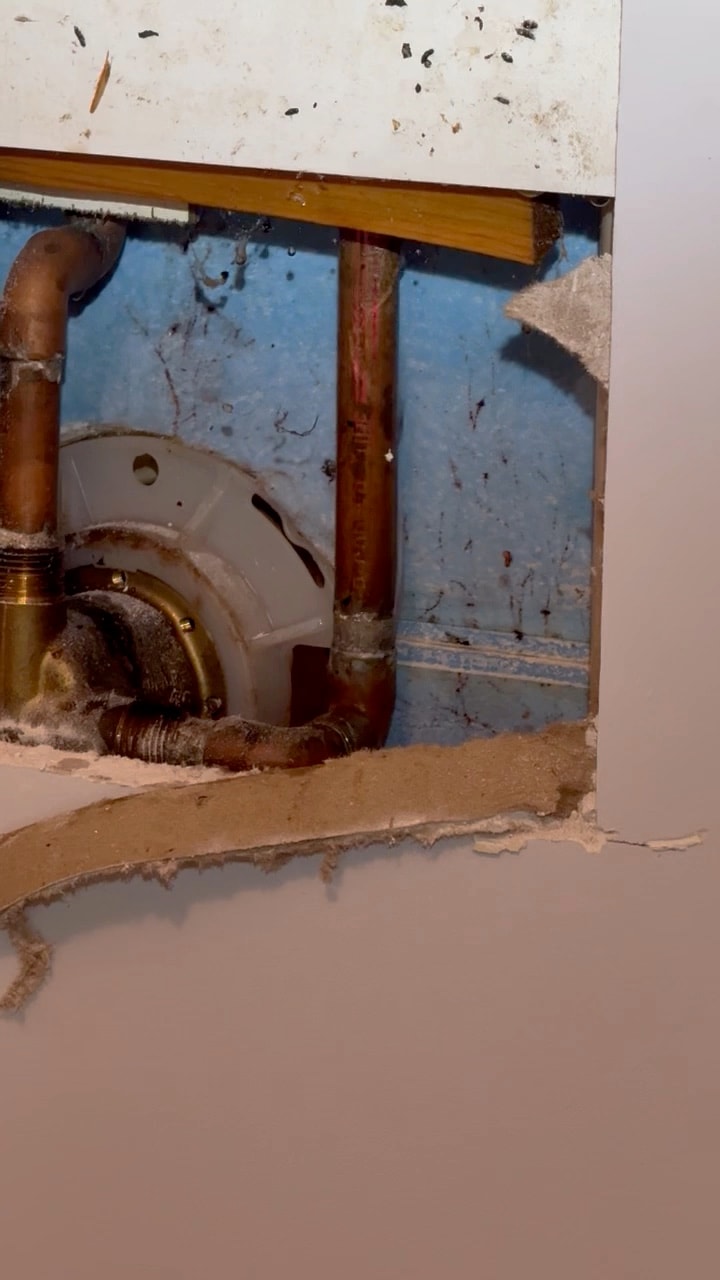Video of a shower mixing valve exposed through a small opening cut in the wall to reach a leak