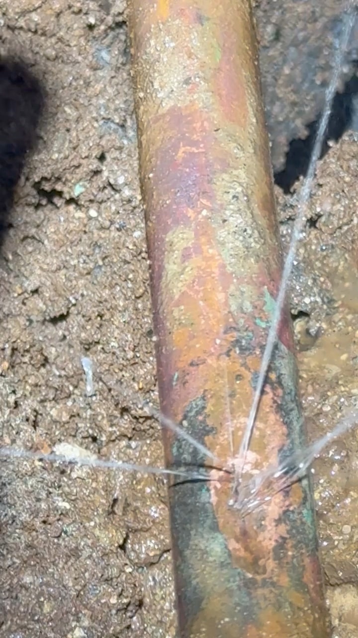 Video of water spraying from pinholes in a buried copper water line that has been dug out