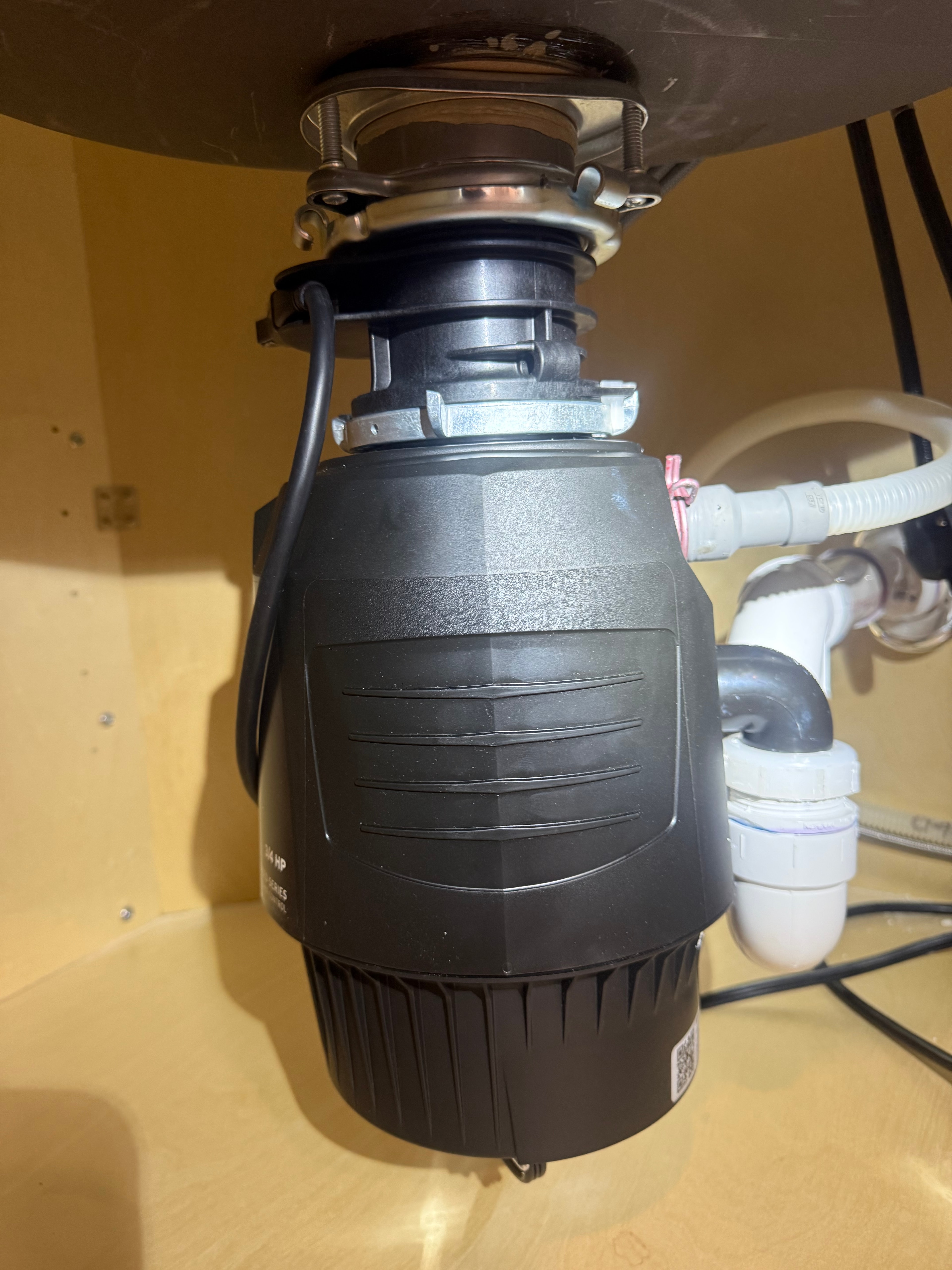 A newly installed garbage disposal unit mounted under a kitchen sink, with the trap and dishwasher hose connected