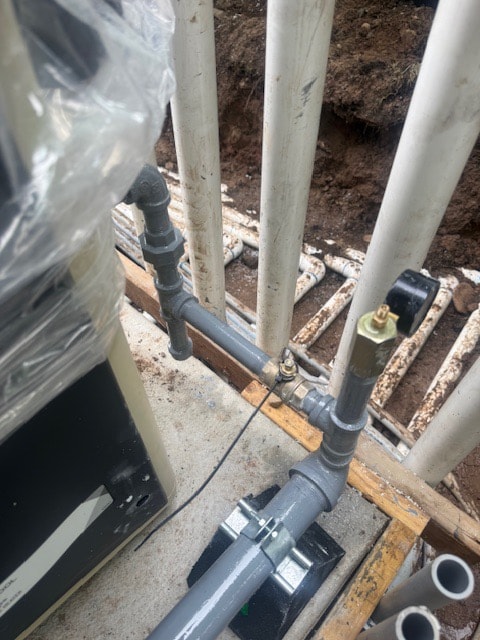 New coated gas piping with a shut-off valve and drip leg run to an outdoor appliance beside an open trench