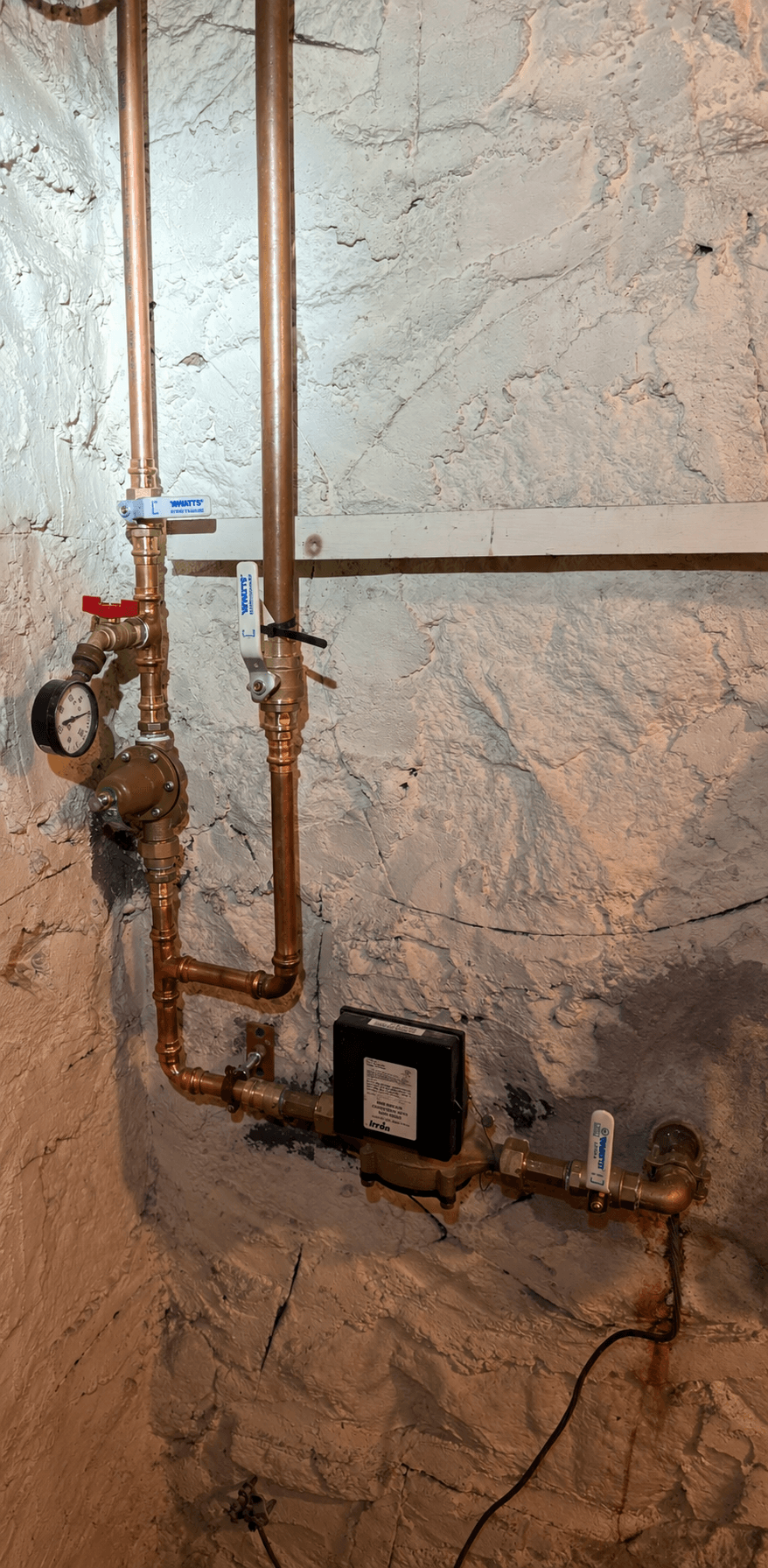 A copper riser with a brass pressure reducing valve, gauge and tagged sprinkler shut-off on a basement wall