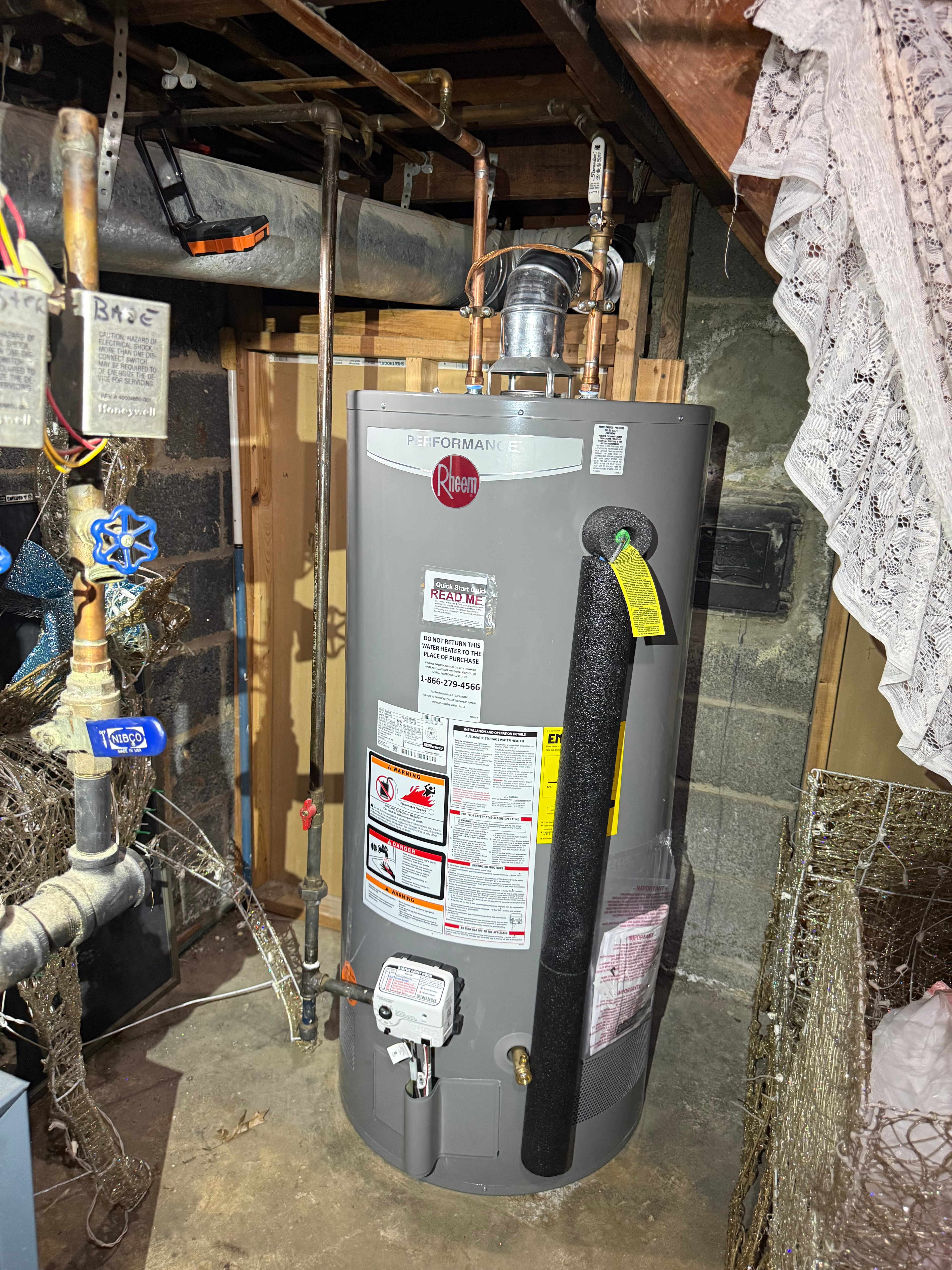 A Rheem gas water heater raised on a timber platform in an older basement, vent connected