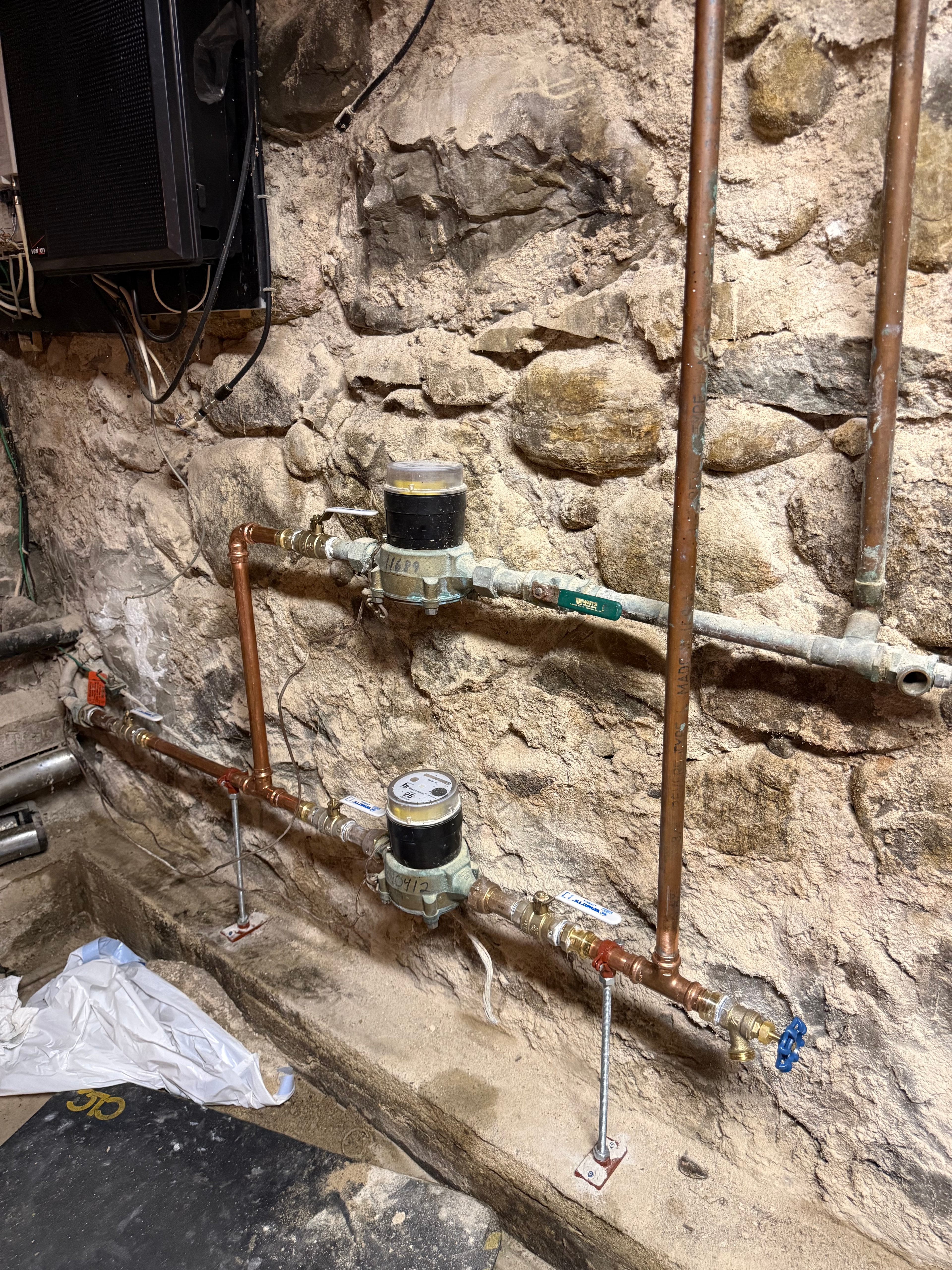 A pair of house water meters on a stone basement wall, brought back into service with new brass valves
